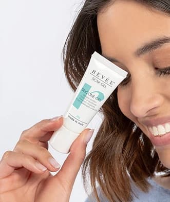 Close-up of a smiling female model holding a Revee Scar Gel tube.