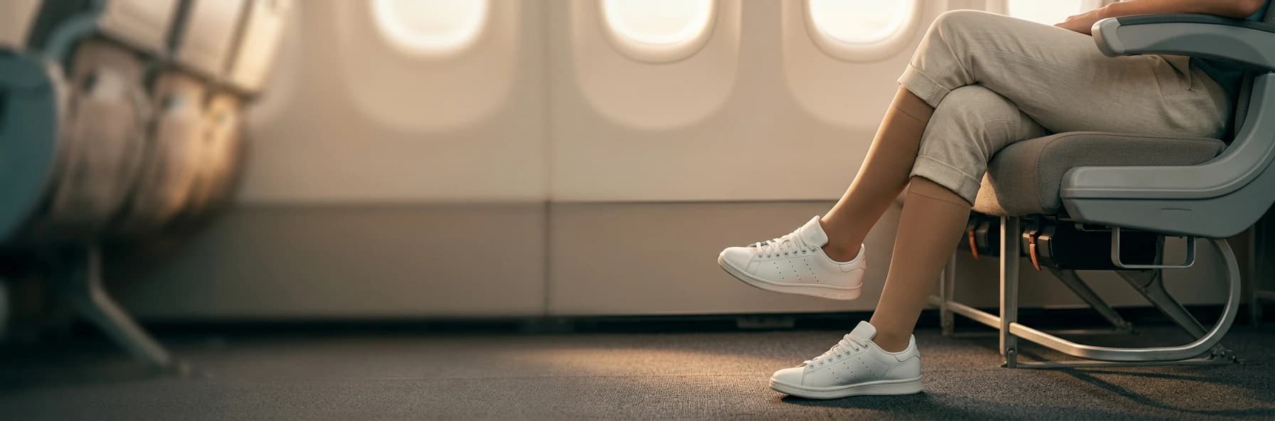 Traveller seated in an airplane window seat wearing skin-tone knee-high compression stockings with white sneakers