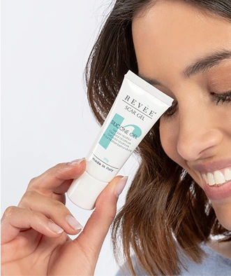 Close-up of a smiling female model holding a Revee Scar Gel tube.